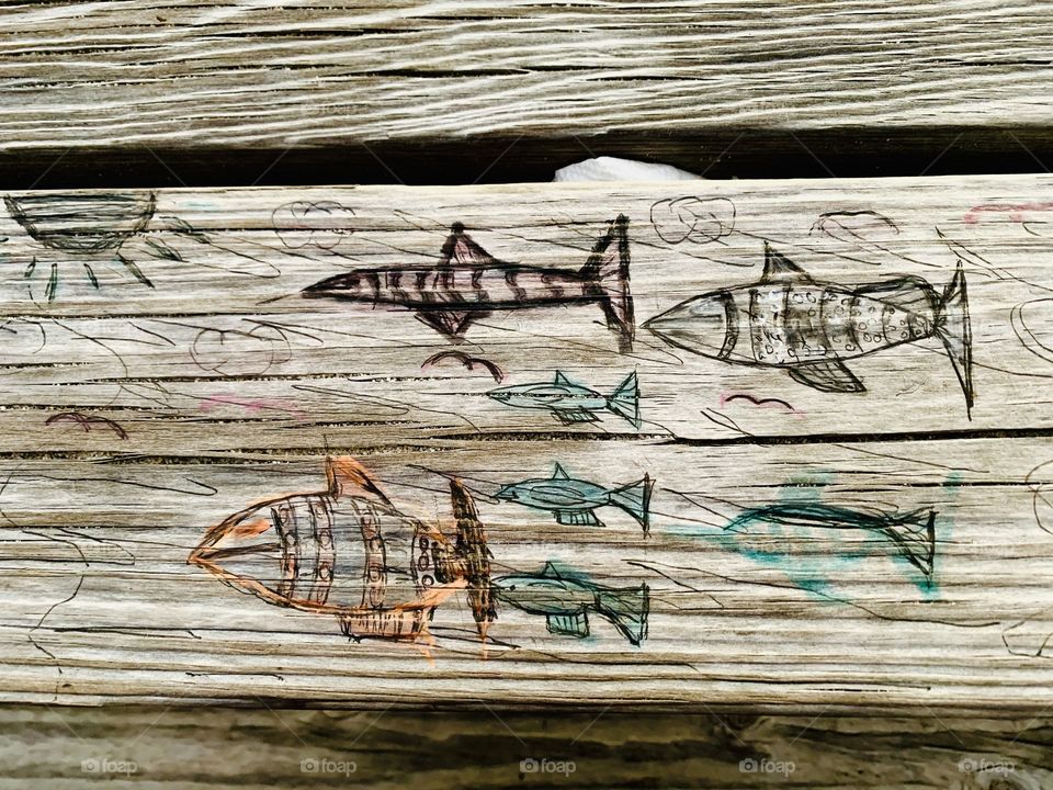 
Someone carved these designs in a wooden picnic table. Carving is the act of fashioning or producing by cutting into or shaping solid material, as wood. a carved design or figure.