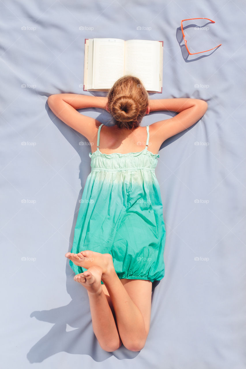 Rear view of a girl reading text book on bed