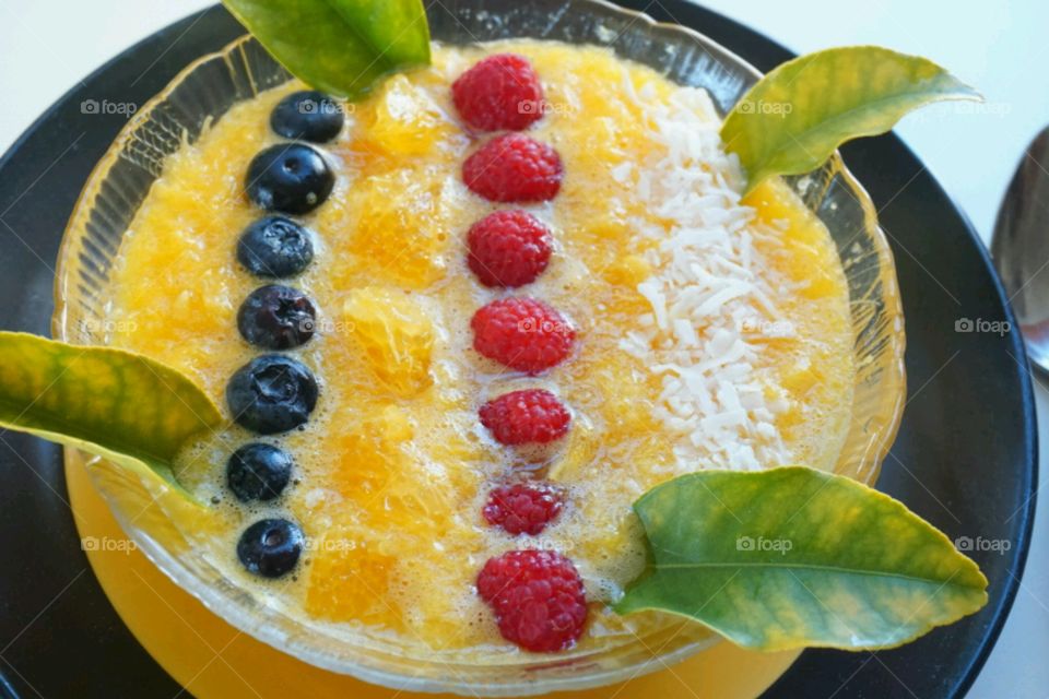 Fresh fruit smoothie - orange smoothie topped blueberries,  raspberries and diced coconut