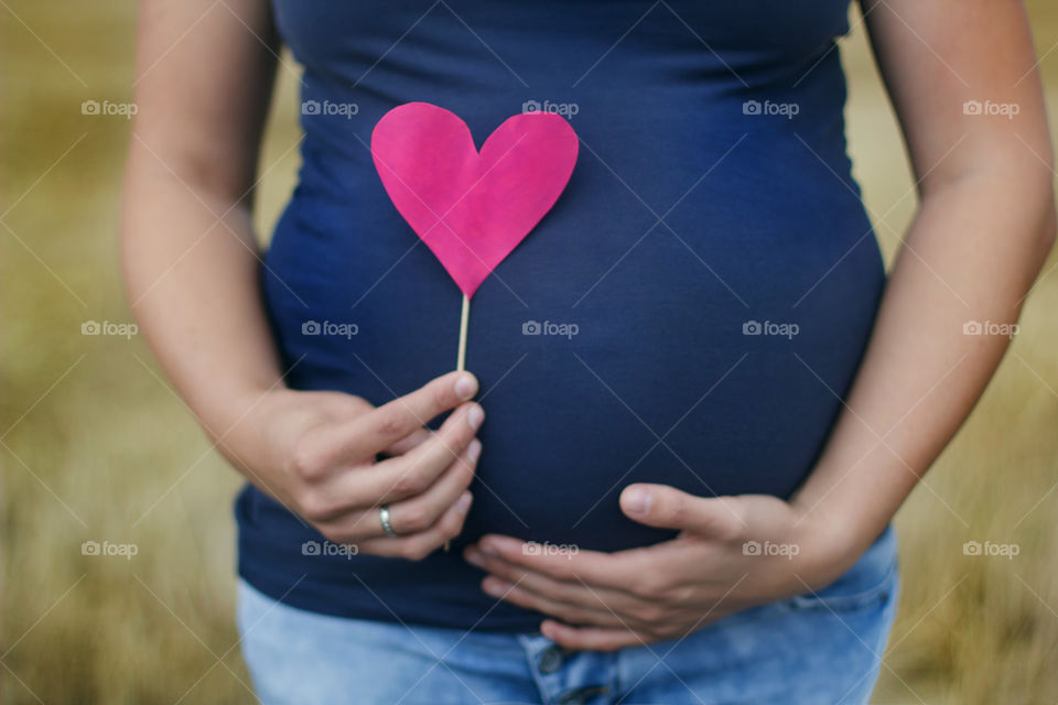 a mother she stroke her babybump and in the other hand she hold a pink heart