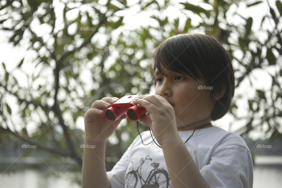 the adventurer, you boy looking through binoculars in the open outdoor with trees background out of focus