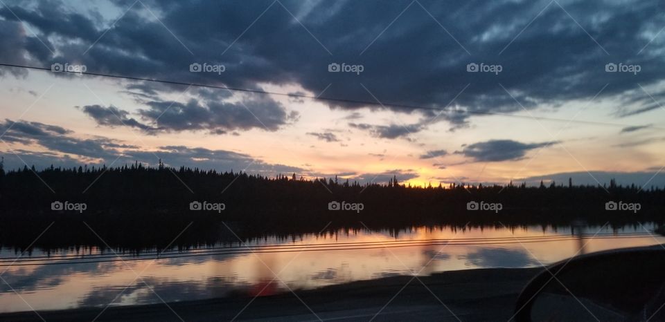 sunset silhouette tree line by water with the last drop of sun in the sky. yellow orange and blue