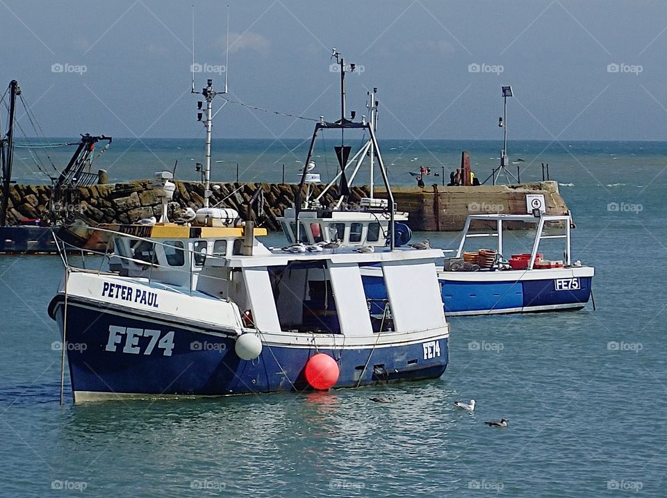 A bright blue fishing boat anchored in the harbor in Folkestone, England on a sunny summer day. 