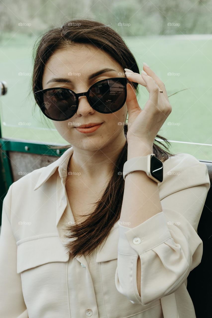 Portrait of one beautiful Caucasian brunette girl in sunglasses with a gentle smile looking at the camera sitting in an open tourist train carriage on a spring day, side view close-up.
