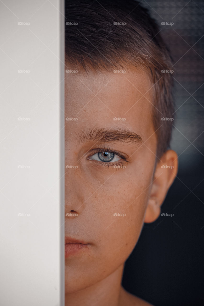 Close-up portrait of young boy behind window frame.
