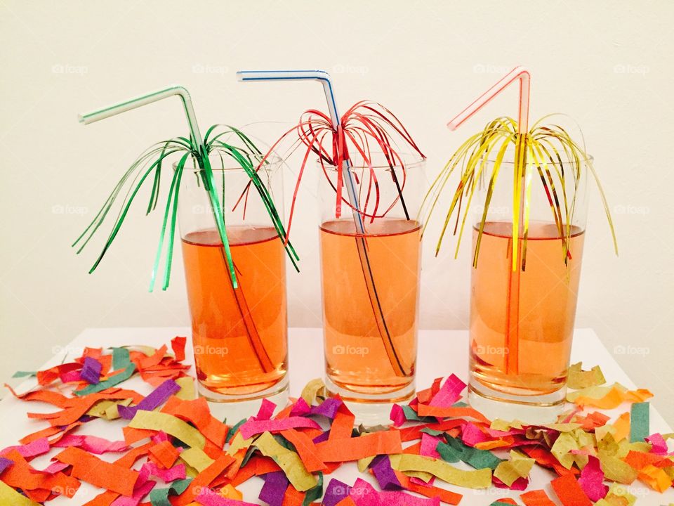 Three cocktails with decorated straws on a table with confetti