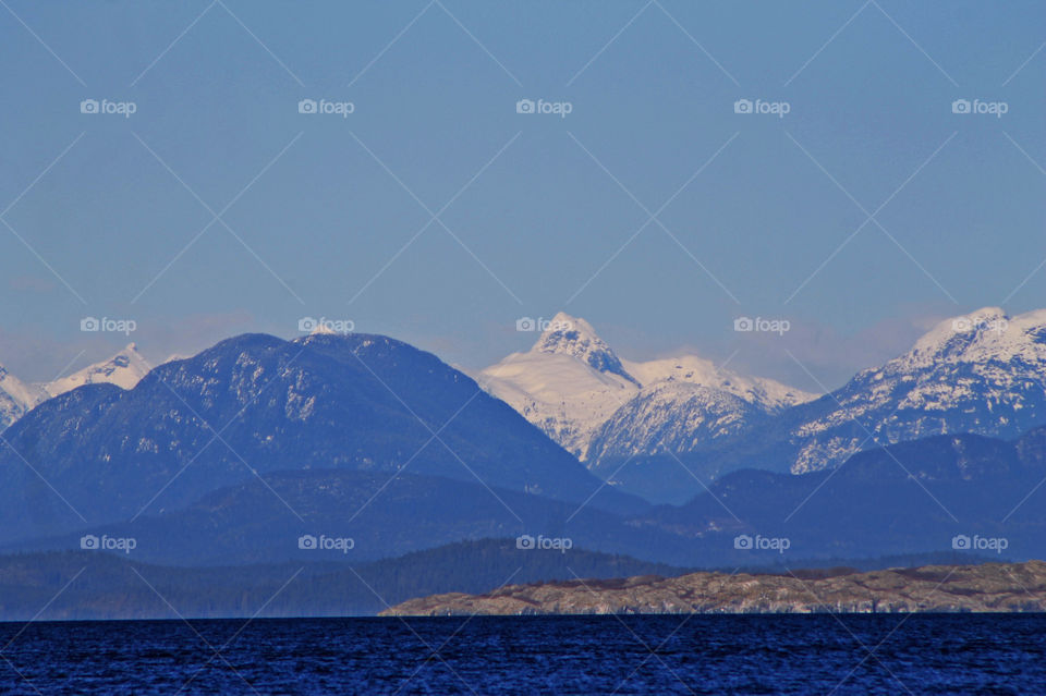 Another rare but welcome sunny winter day in Beautiful British Columbia. This shot is the Mainland mountains viewed from Vancouver Island. There is a wisp of clouds over the mountain caps the dark blue ocean of the Salish Sea in the foreground. 