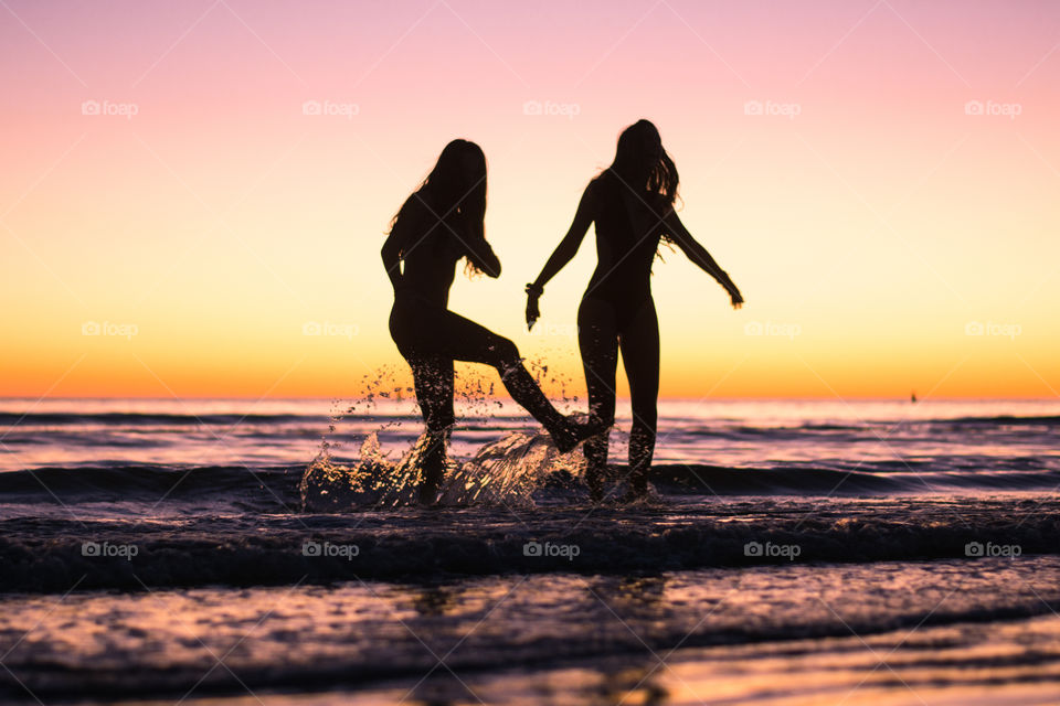 Two girls splash around in the ocean as the sun sets behind in beautiful colors!