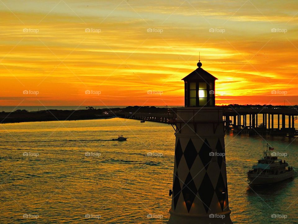 A silhouette lighthouse with its beacon light on during a beautiful sunset over the Gulf of Mexico. The lighthouse directs inbound ships to safe anchoring