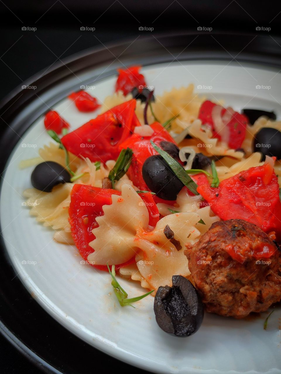 FARFALLE paste.  Red tomatoes.  Olives.  Chopped greens.  Grated cheese.  Pieces of garlic.  Meatballs