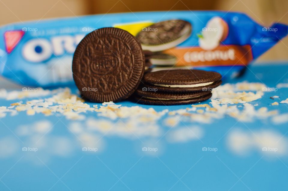 A stack of coconut Oreo thin cookies on a blue background with coconut shreds