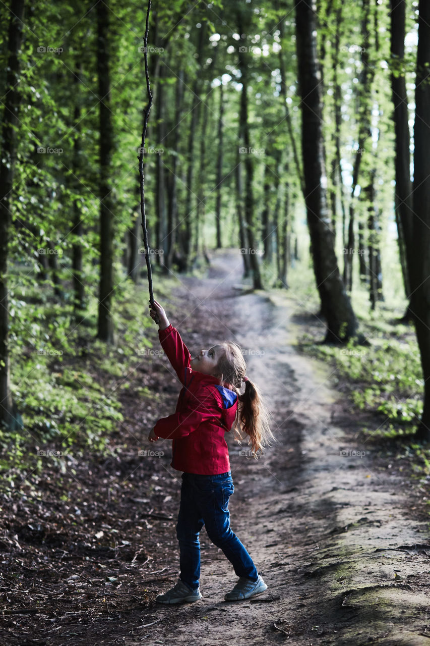 Little girl playing with stick in a forest on country road