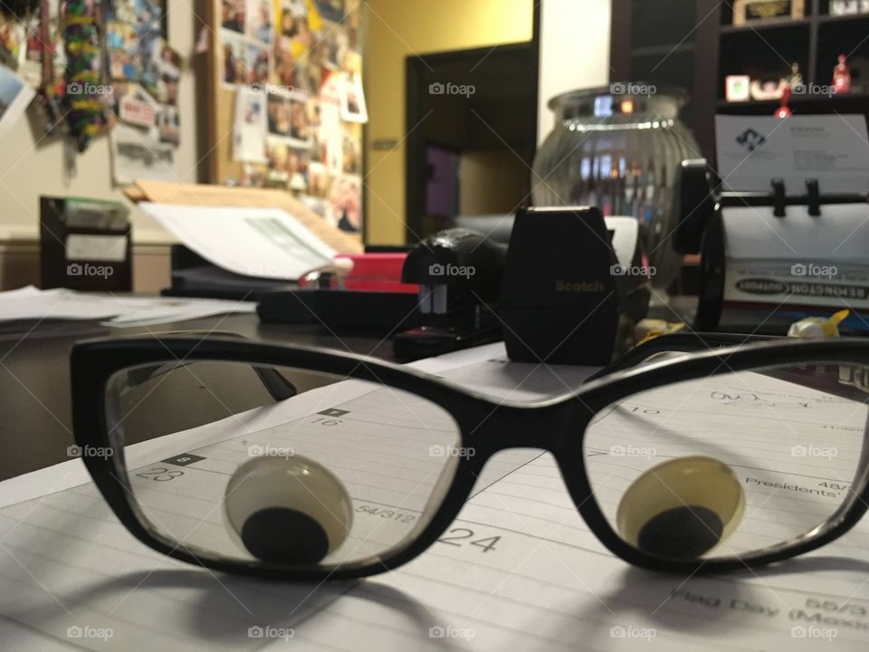 Googley eyes inside black glasses on a desk 👓