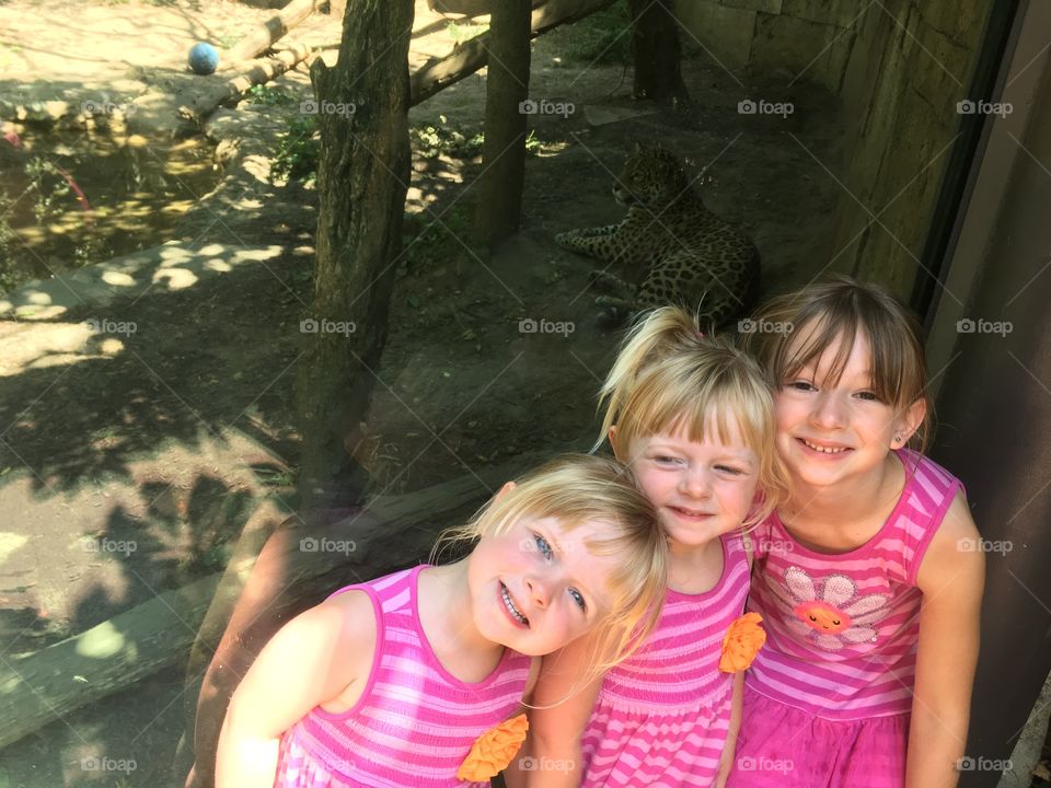 Sisters having fun at the zoo with big cat in background. 