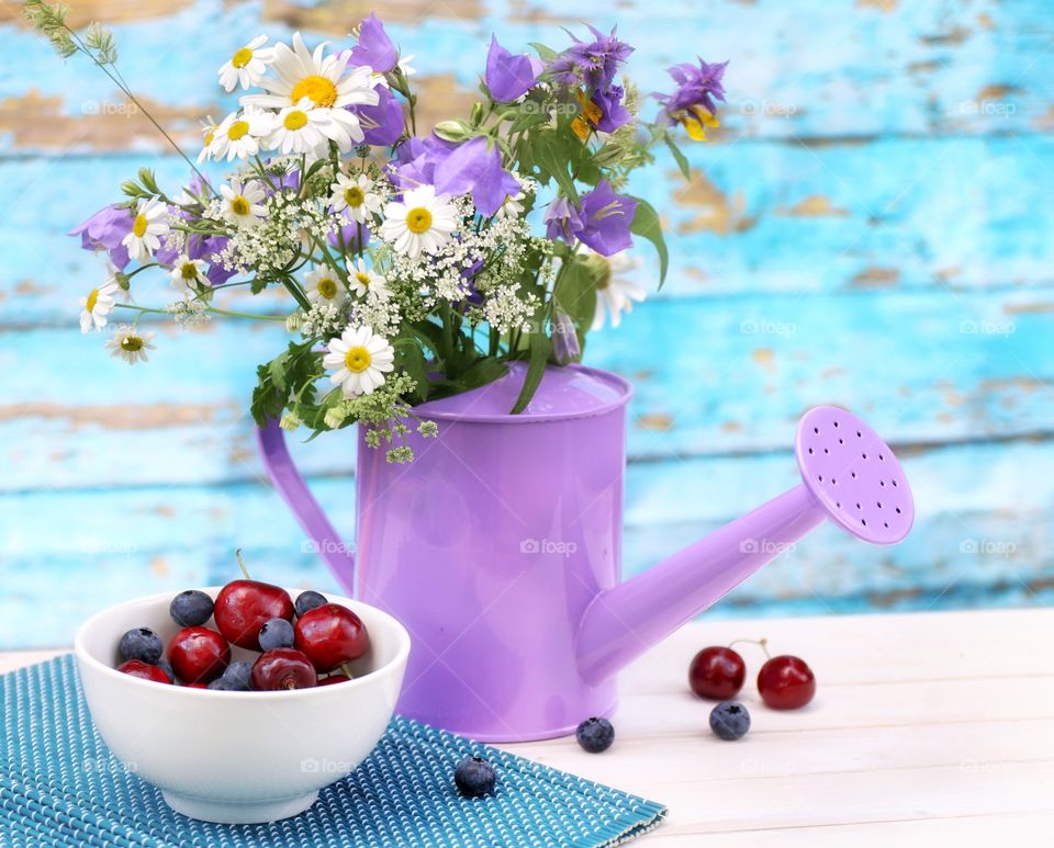 Wildflowers in a watering can and berries of cherries and blueberries