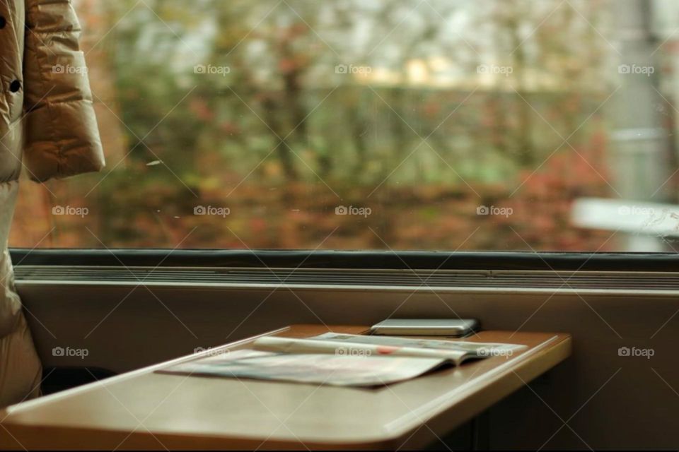 Commuting on the train with a newspaper and mobile phone on the table in front of the train window 