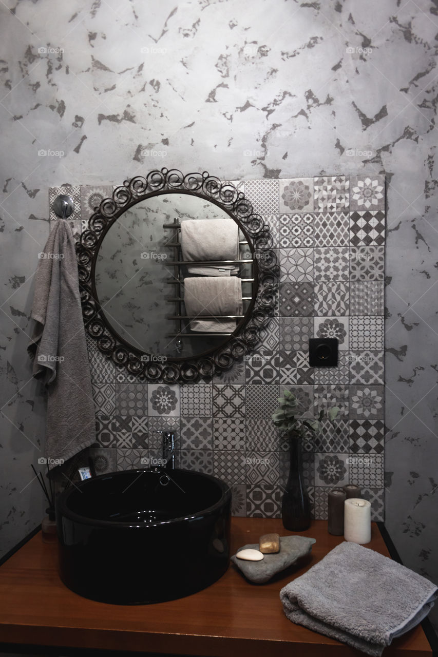 Grey concrete designer bathroom with antique circle mirror, black sink and mosaic tile 