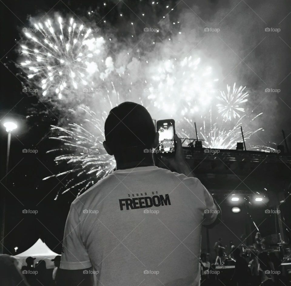 A black and white photo of a man enjoying a July 4th fireworks celebration.