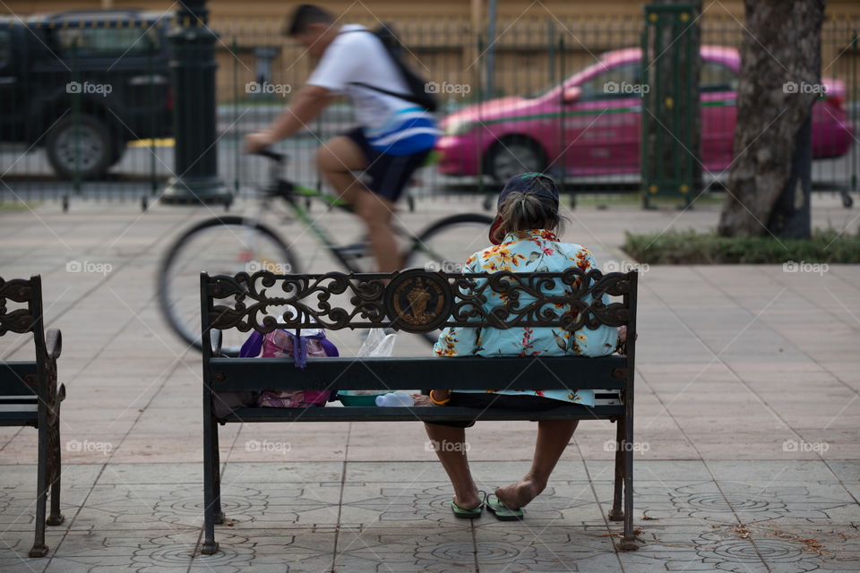 Old woman sitting in the park and the bicycle pass by