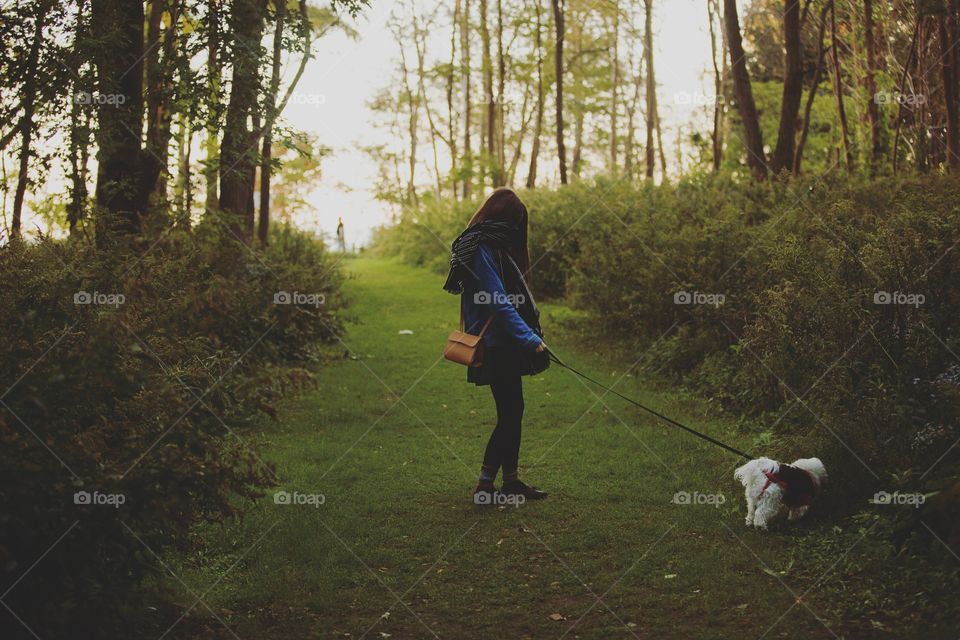 Girl walking her puppy into a forest at sunset