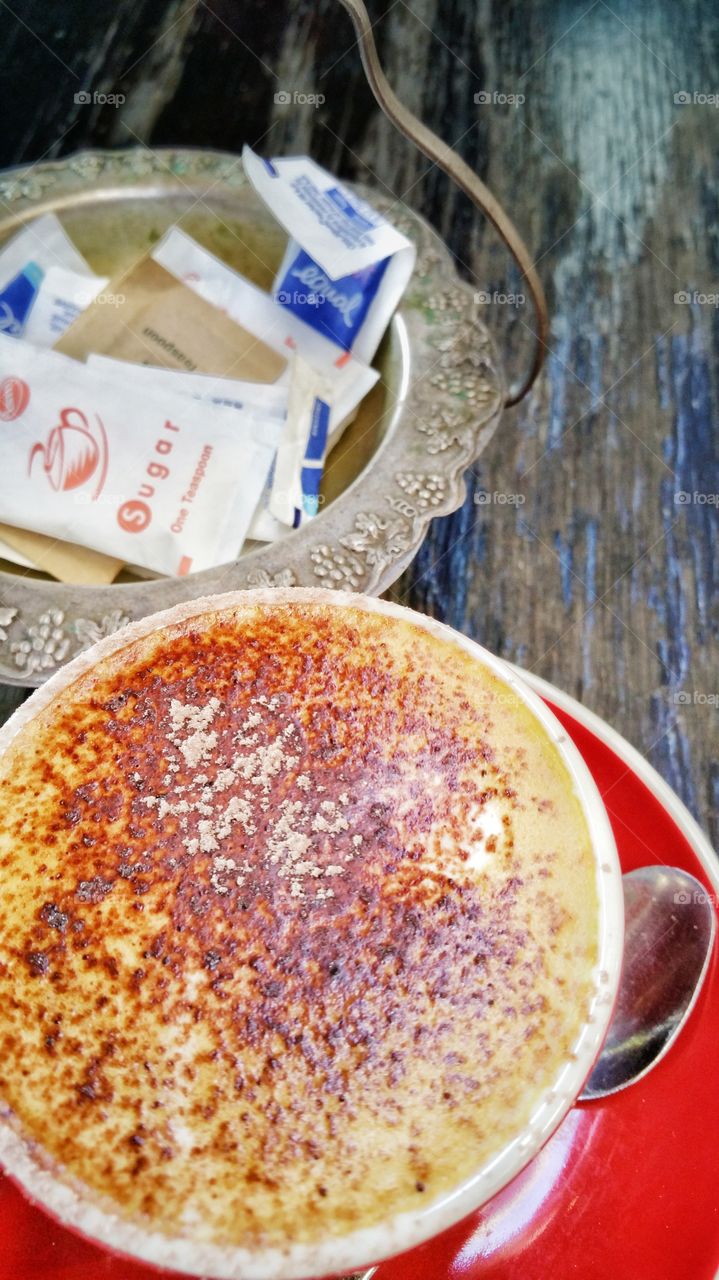 Cappuccino coffee with a selection of sugars in the background. Cappuccino is an Italian coffee beverage that is traditionally prepared with double espresso, and steamed milk foam.