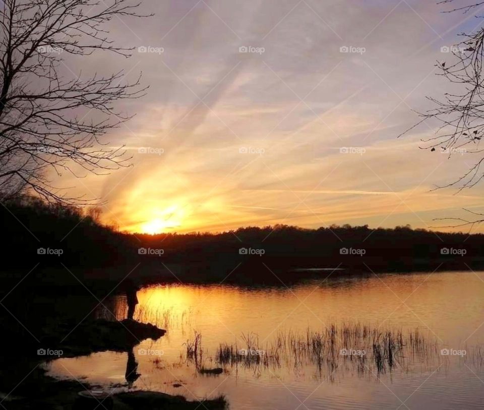 Silhouette of a man standing by the lake at sunset