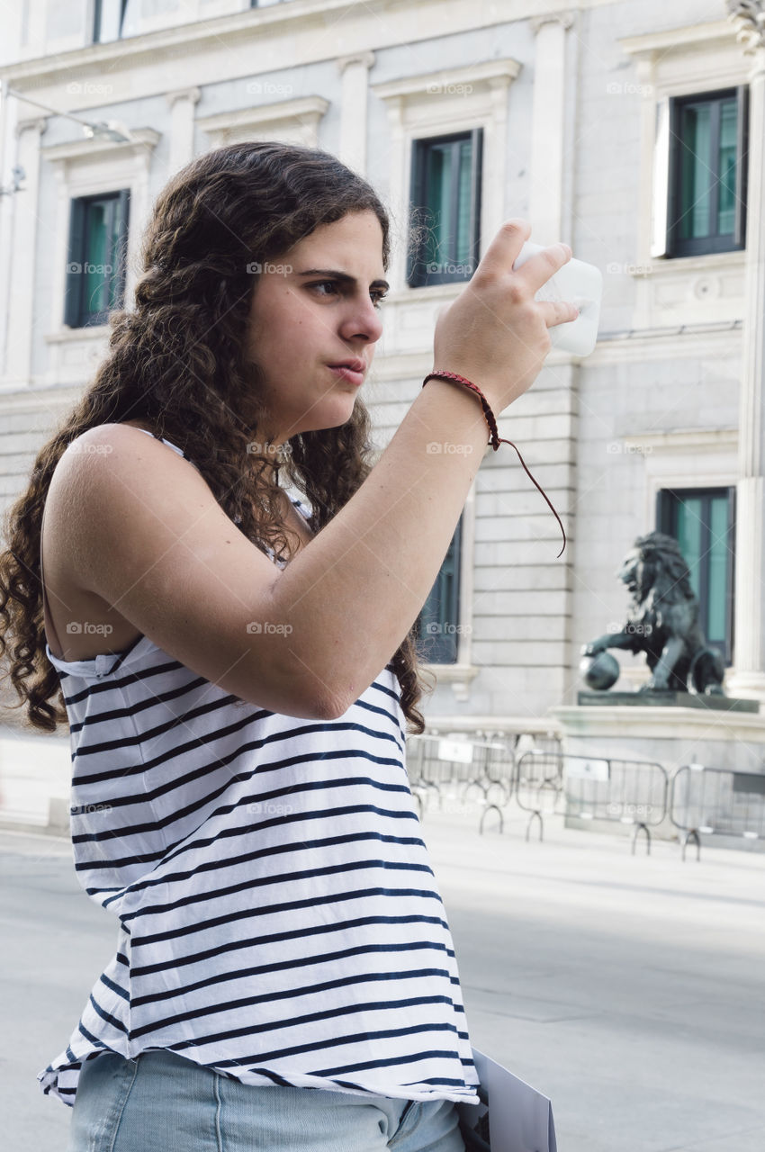 Young adult taking photos with her smartphone in the street. Madrid