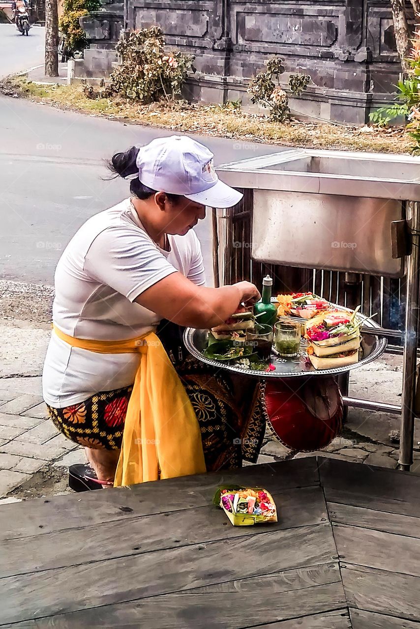 Denpasar, Bali, Indonesia - September 25, 2023: A woman is placing offerings in front of a shop which is traditional in Bali, Indonesia