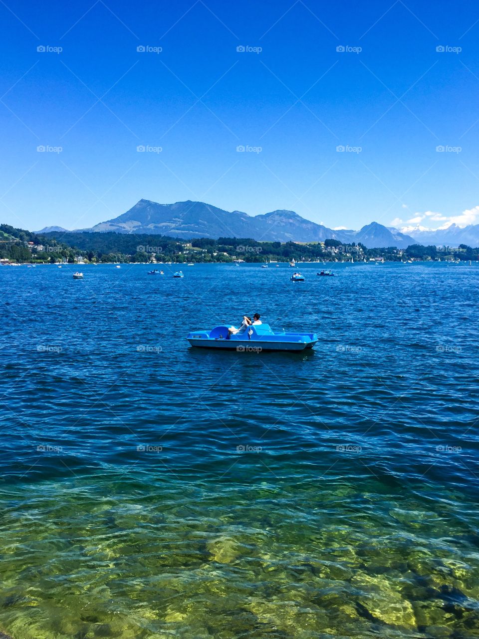 on the clear blue water, there were many people go around with boats pedaled on foot, can be seen rocks underwater . there are undulating mountains , blue sky . good weather