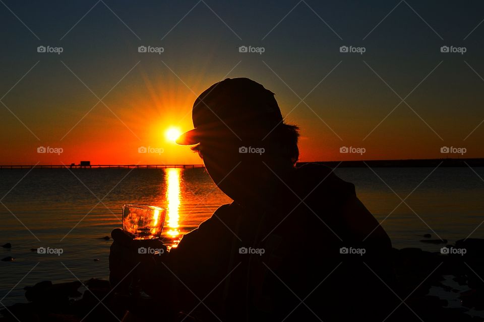 A glass of wine at day's end... A young man enjoying the end of a day at sunset with a glass of red wine, south Australia beach