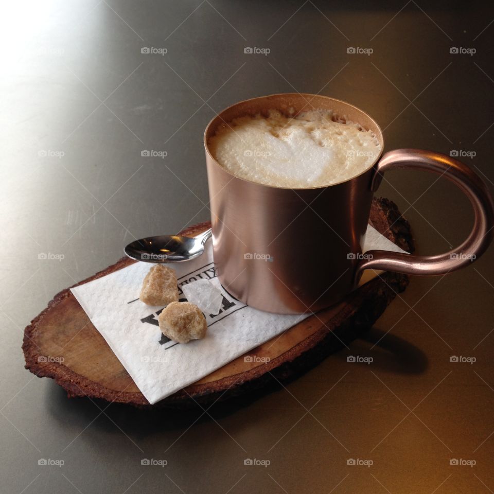  Latte served in a metal coffee mug on a wood plate with pieces of cane sugar