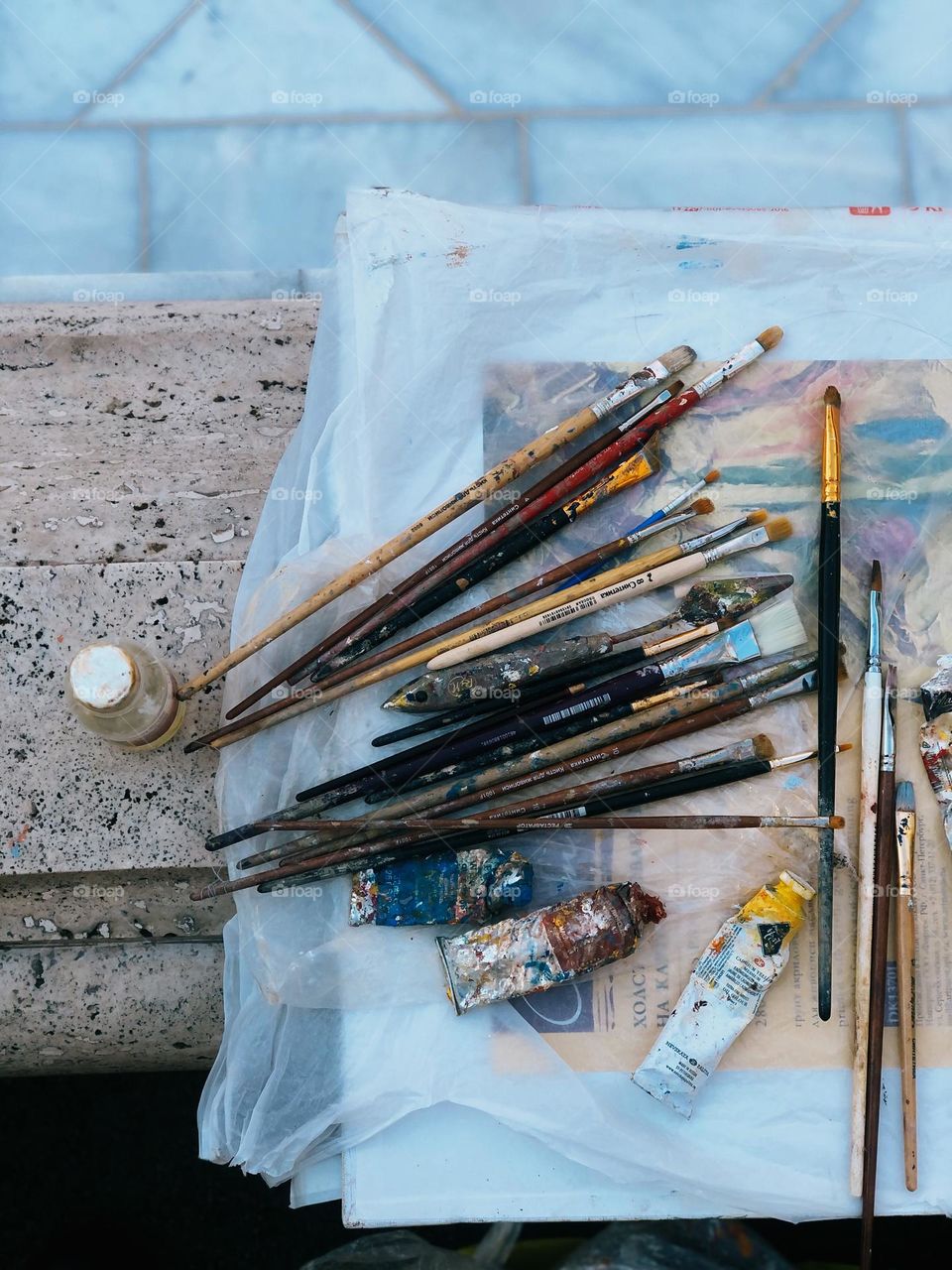 Colored pencils, brushes, paints lie on the concrete table, nobody 