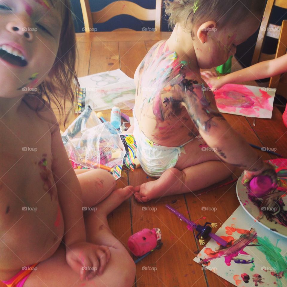 Two little girls playing with paints on wooden table