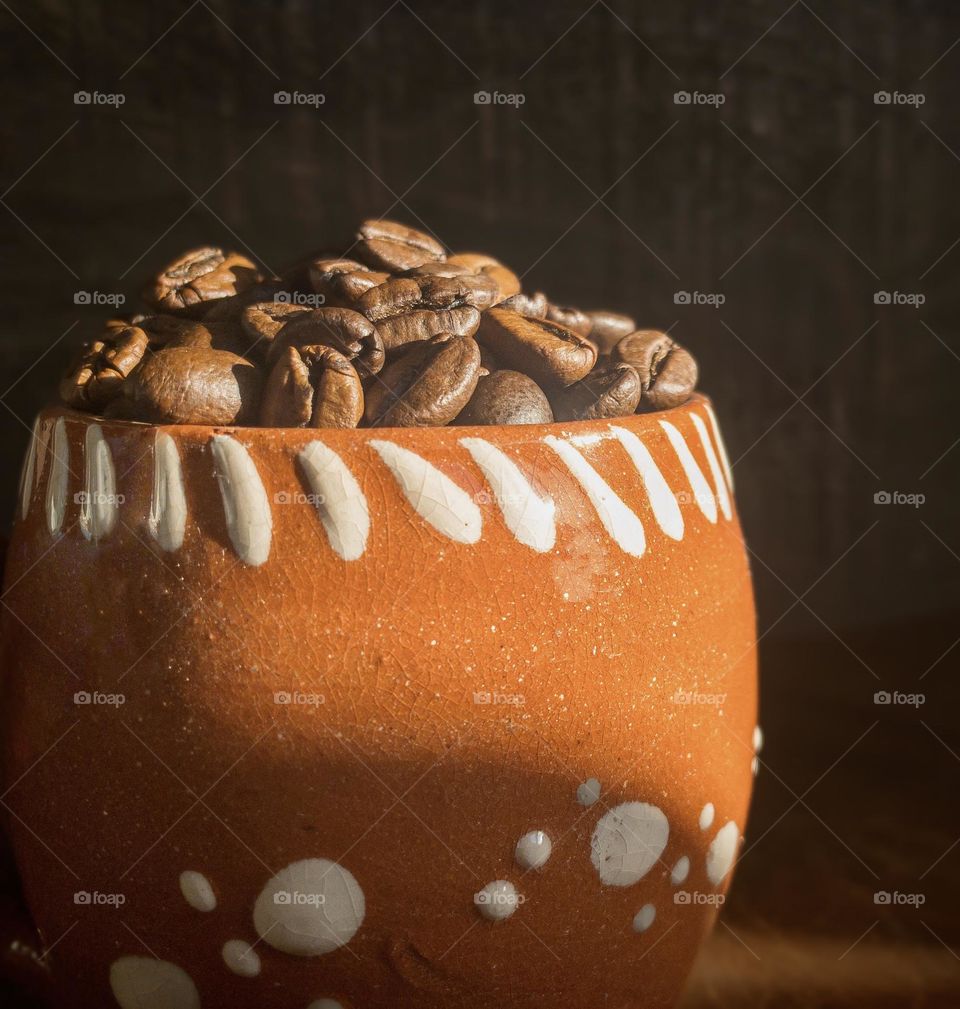 A terracotta mug full of coffee beans caught in a shaft of sunlight 