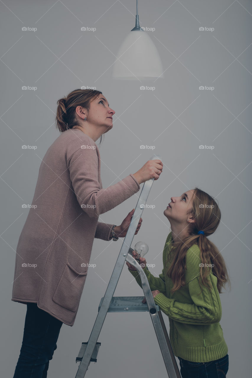 Mother and daughter standing on ladder changing light bulb