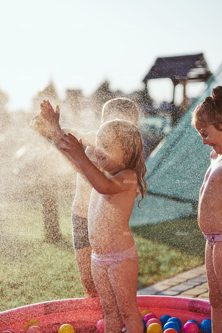 Little cute adorable kids enjoying a cool water sprayed by their father during hot summer day in backyard. Candid people, real moments, authentic situations