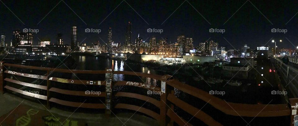 A gigantic panoramic shot of the illuminated New York City at night seen from the “Pulaski Bridge” on the “Greenpoint”, Brooklyn side looking across Newtown Creek at the LIC, Queens and the Manhattan skyline behind it. 2022. Hypnotic Productions