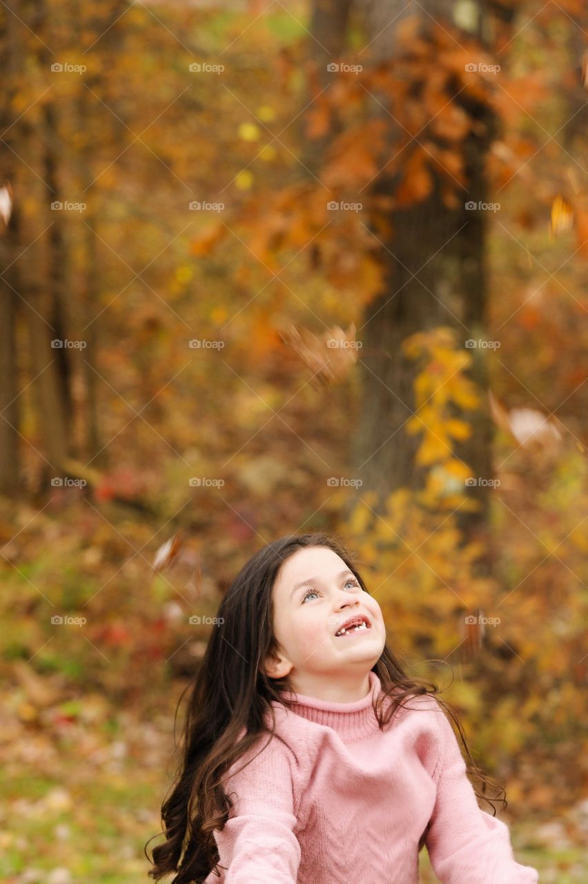 Happy little brunette girl laughing and smiling and throwing autumn leaves in pink sweater