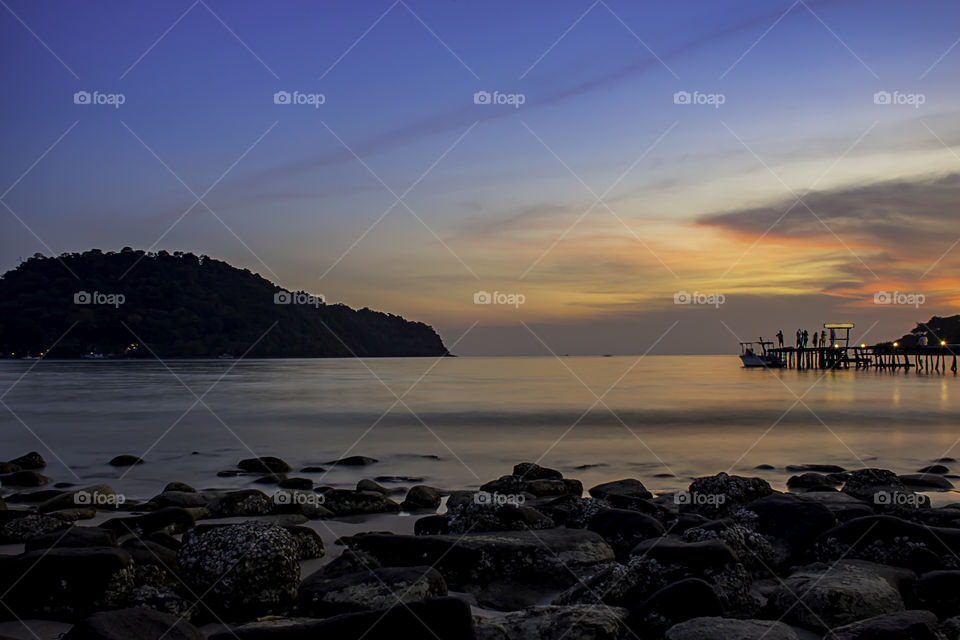 The sunset behind the island in the sea and the shadow of the tourists on the wooden bridge at Koh Kood, Trat in Thailand.