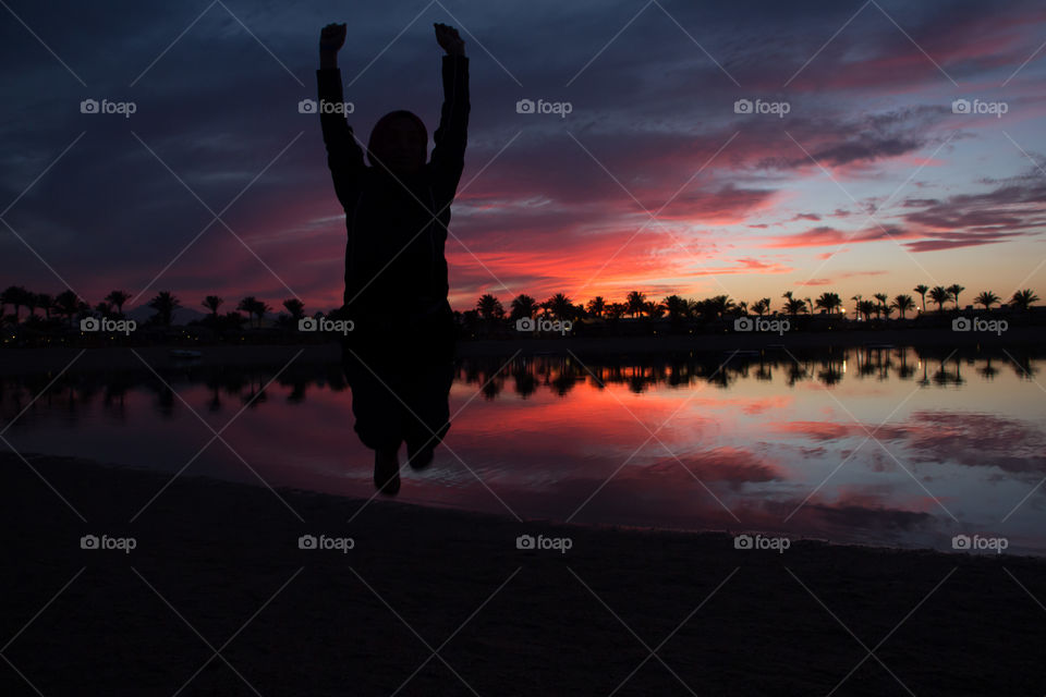 A silhouette scene of a person jumping in front of a beautiful sky and palm view, at twilight timing.