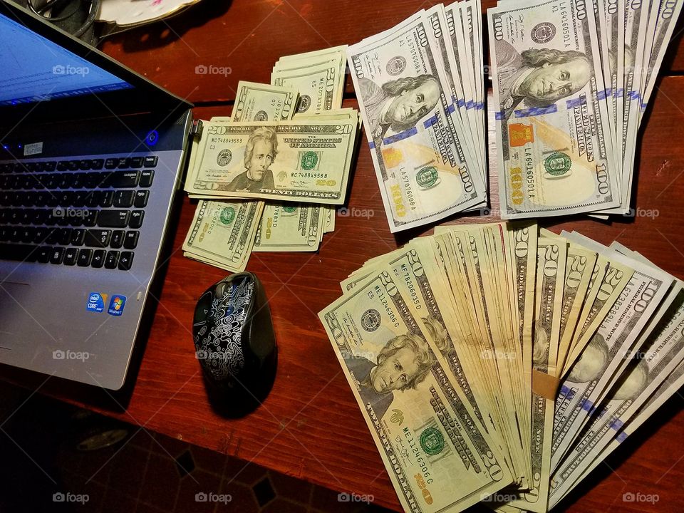 U.S. Paper currency spread out near laptop, adding up paper money on desk. $20s & $100s.