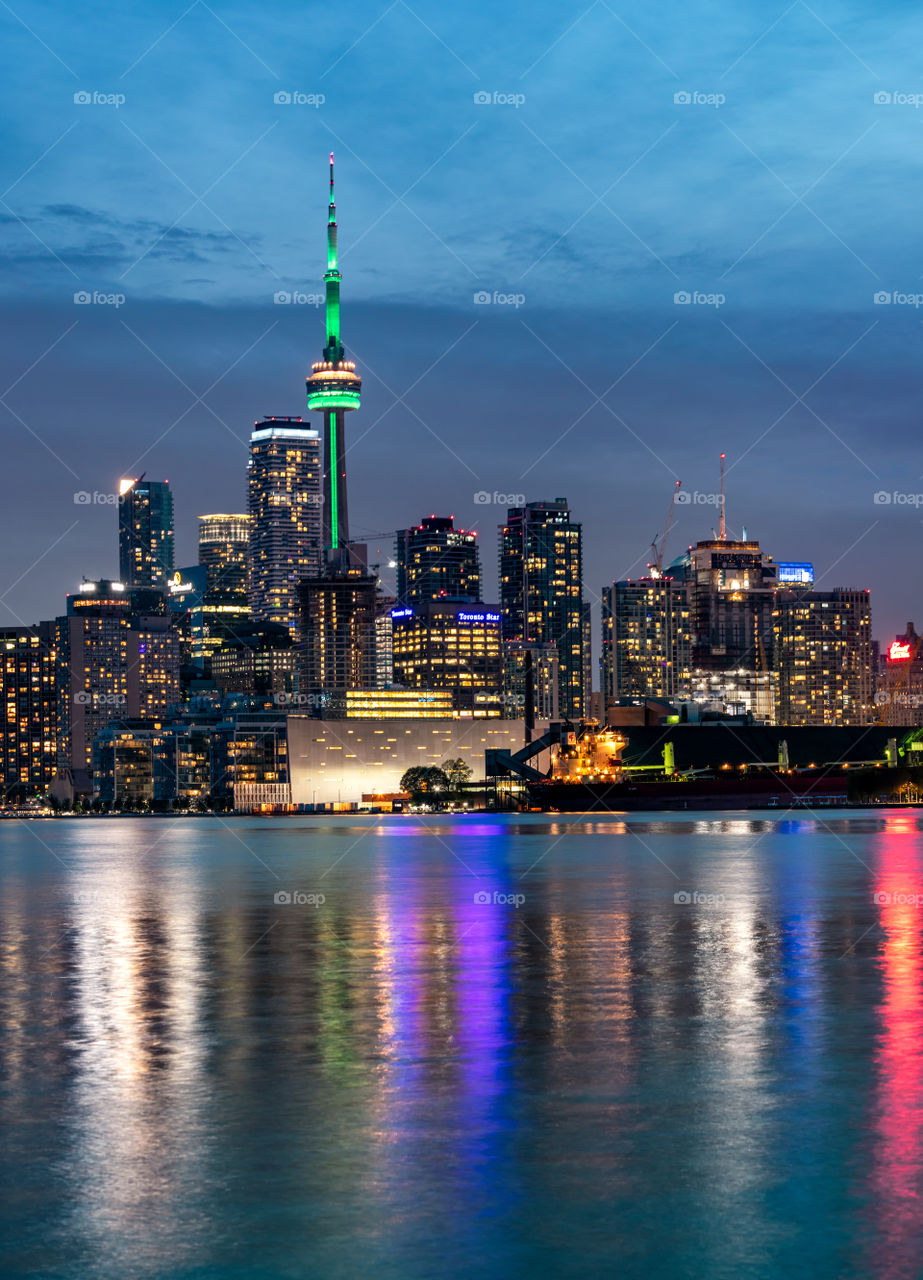 Toronto skyline lit up during blue hour, with all of the building lights reflecting different colors in Lake Ontario. 