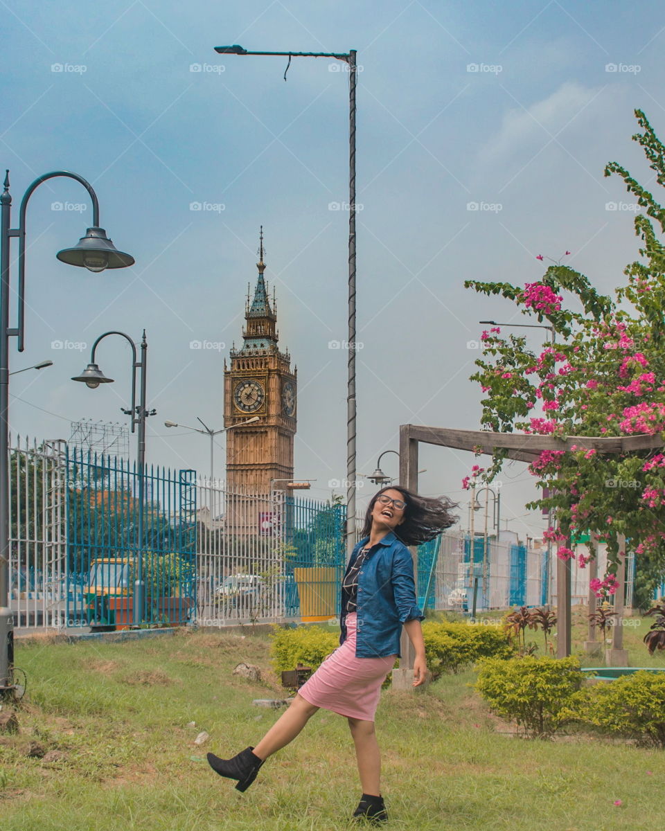 A girl is standing in front of the big ben (Kolkata, India) under the bright blue sky on a bright sunny day of summer.