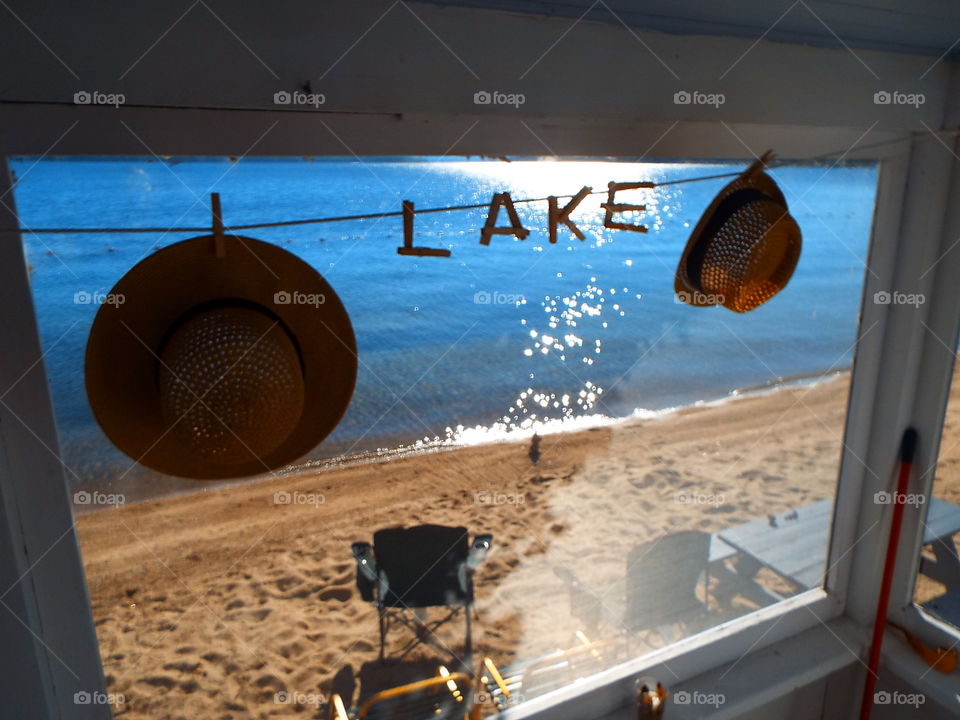 Straw hats hanging on screened porch clothesline looking out at beach and lake in front of cottage