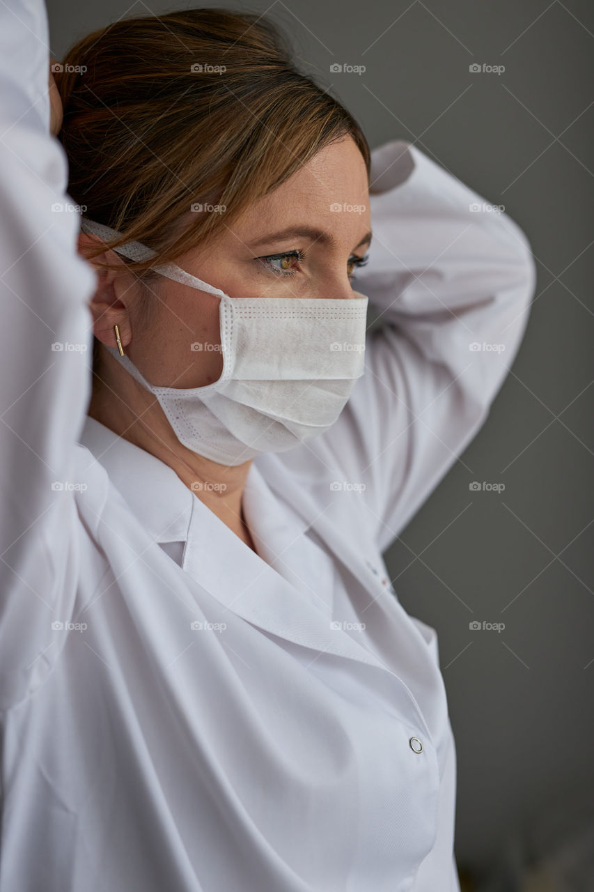 Doctor with face covered with mask. Portrait of young woman wearing the uniform, cap and mask to avoid virus infection and to prevent the spread of disease. Real people, authentic situations