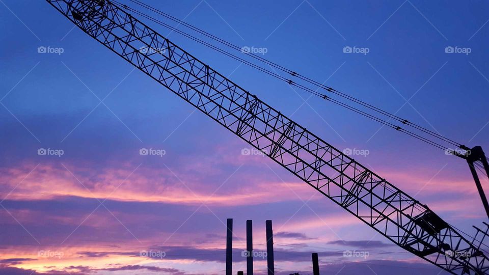 silhouette of crane overlooking a construction site at dusk with beautiful blue sky and pink and purple overcast