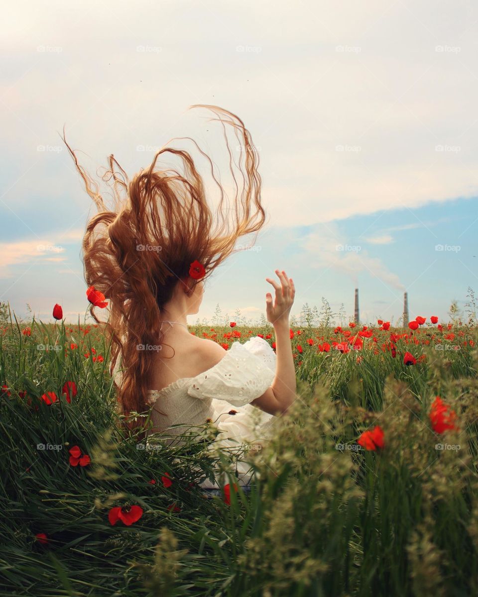 A girl in a white dress in a field of poppies against the background of a thermal power plant
