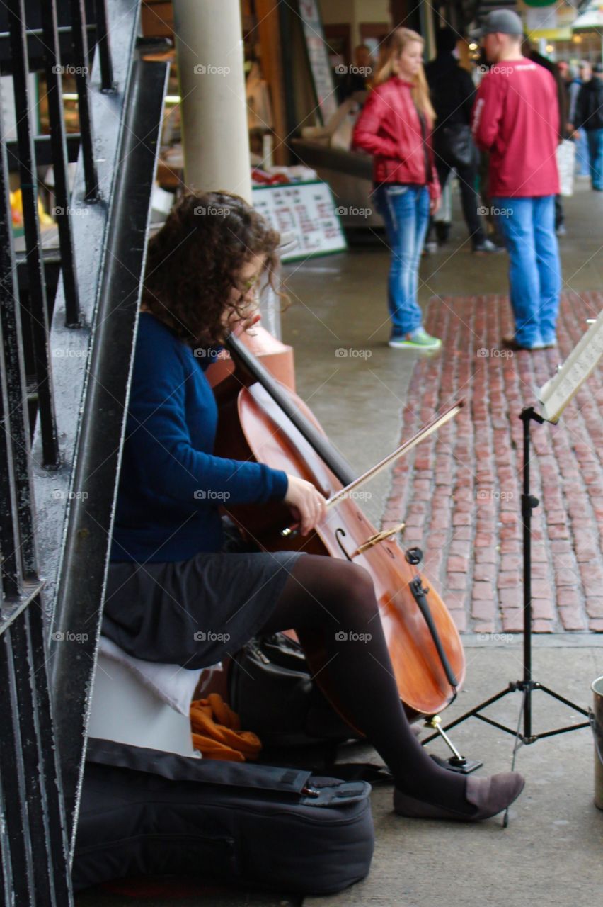 Female street performer plays the cell under an iron stairway in an open marketplace