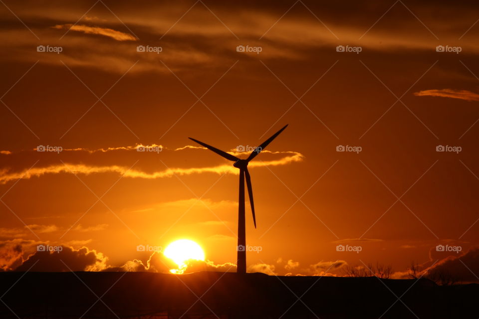 Back-lit wind turbine at sunset in Salento, Puglia, Italy. Orange sky with some clouds.