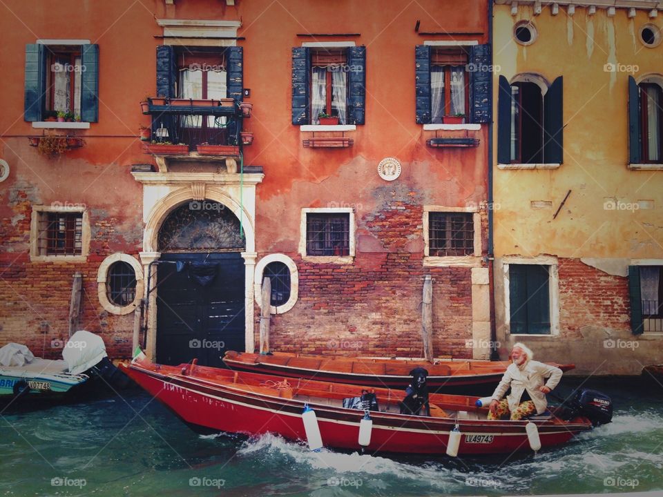 Smiling man having a walk together with his dog friend in gondola down canal in Venice. 